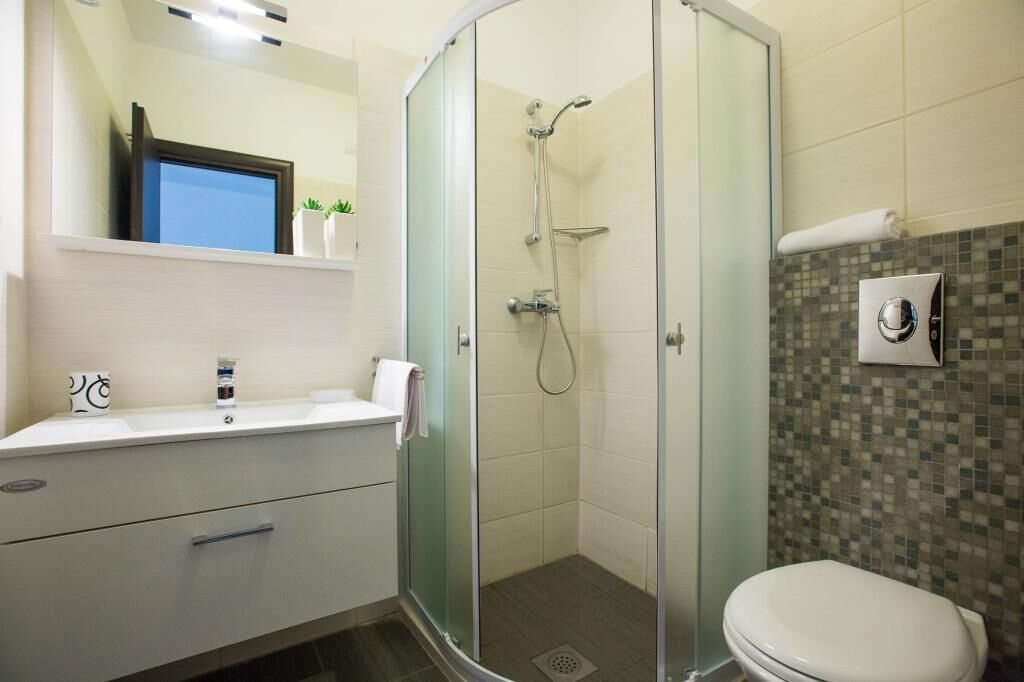 A modern bathroom with a glass-enclosed shower, a white sink with a mirror, and a tiled shower wall.