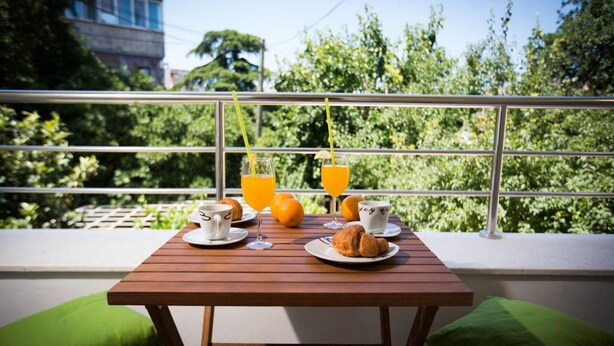 A balcony with a wooden table set for breakfast, including croissants, orange juice, and a cup. - Villa Mia (Dubrovnik)