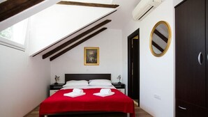 A bedroom with a red bedspread, a black headboard, a framed picture on the wall, a mirror, and a wardrobe. - Villa Mia (Dubrovnik)