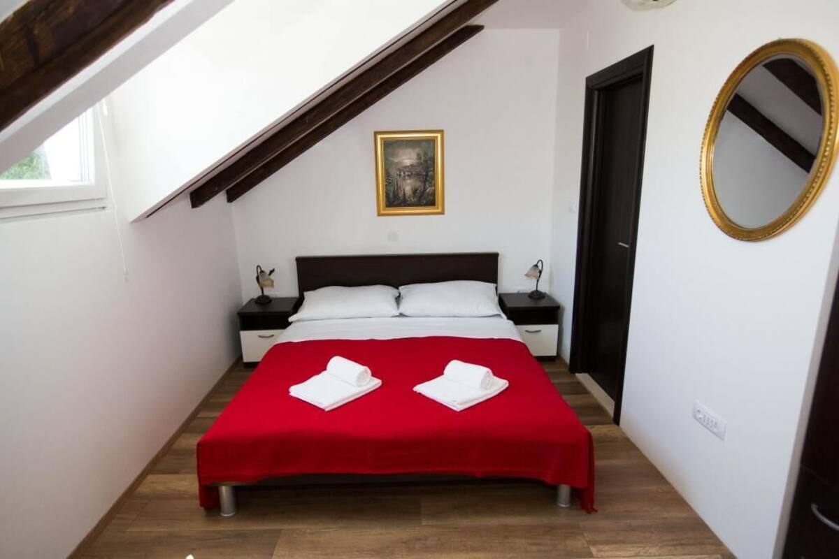 A bedroom with a bed, a nightstand, a bedside table, a framed picture on the wall, and a mirror.