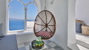 Een kamer met een hangstoel, uitzicht op zee, een bed en een kleine tafel met een karaf en fruit.
