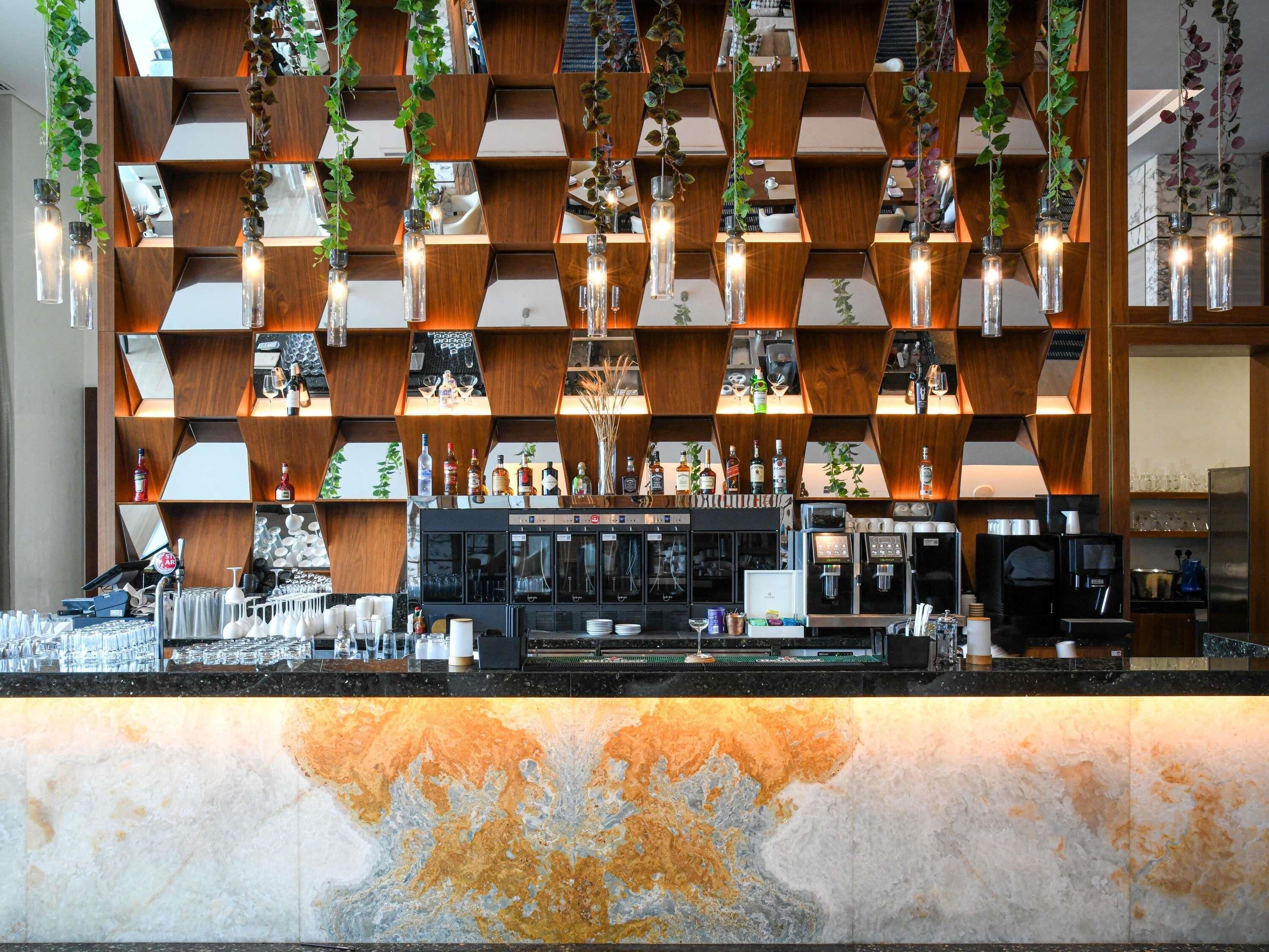 A bar area with a modern design, featuring a geometric wooden wall, hanging plants, and a marble countertop.