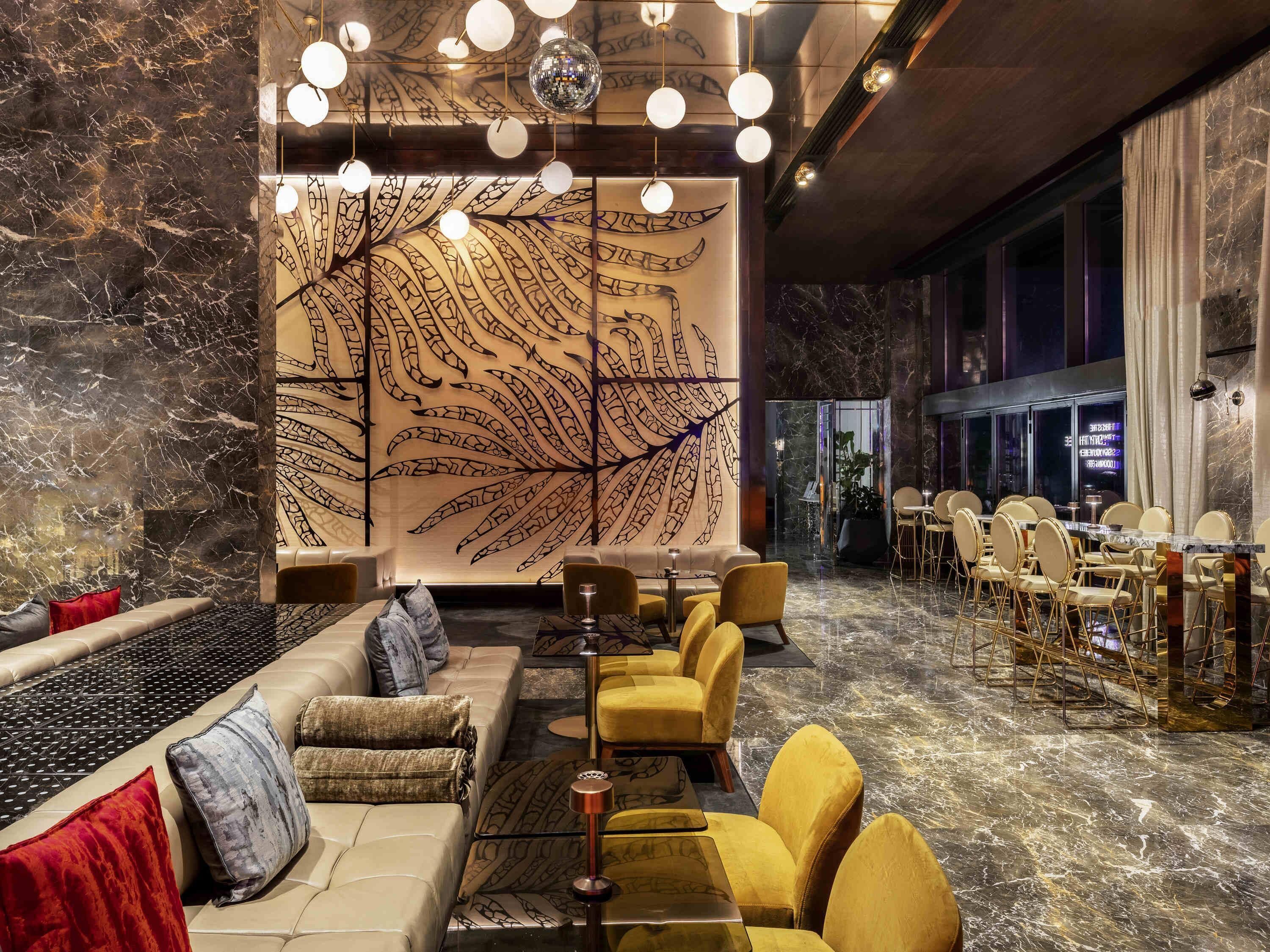Un intérieur moderne comprenant un espace salon, un mur décoratif orné de motifs de feuilles et un coin repas avec des tables et des chaises.