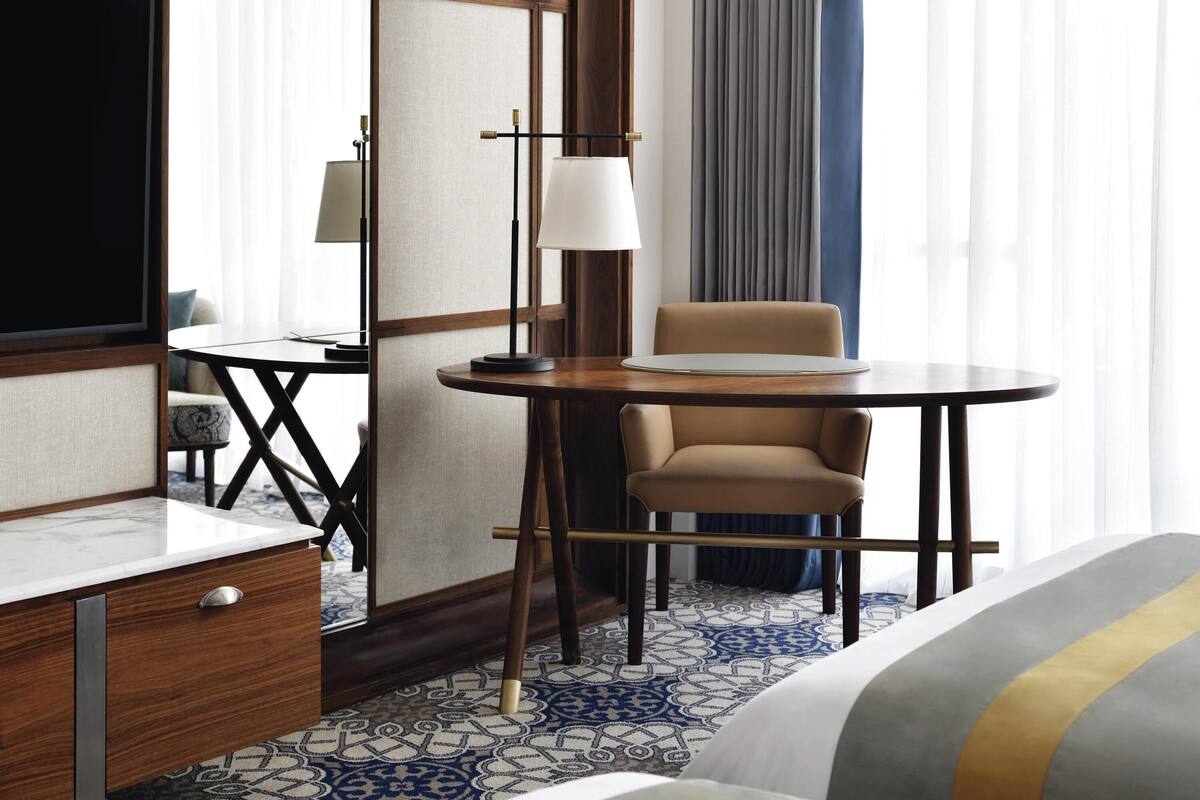 Una habitación de hotel con cama, escritorio, silla, mesa redonda y lámpara.