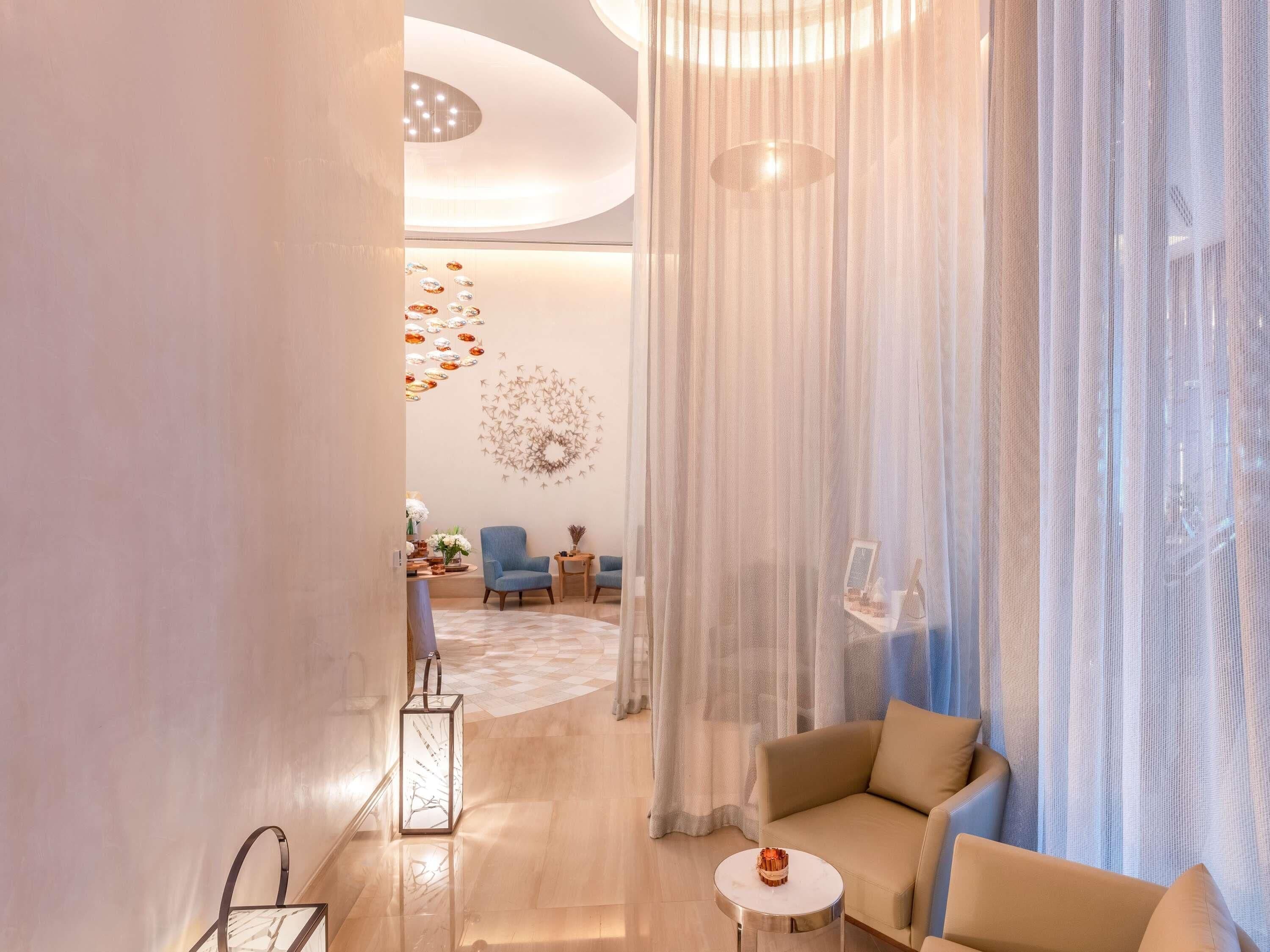A modern hotel lobby with a seating area, a decorative wall, and a large window with sheer curtains.