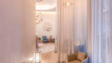A modern hotel lobby with a seating area, a decorative wall, and a large window with sheer curtains.