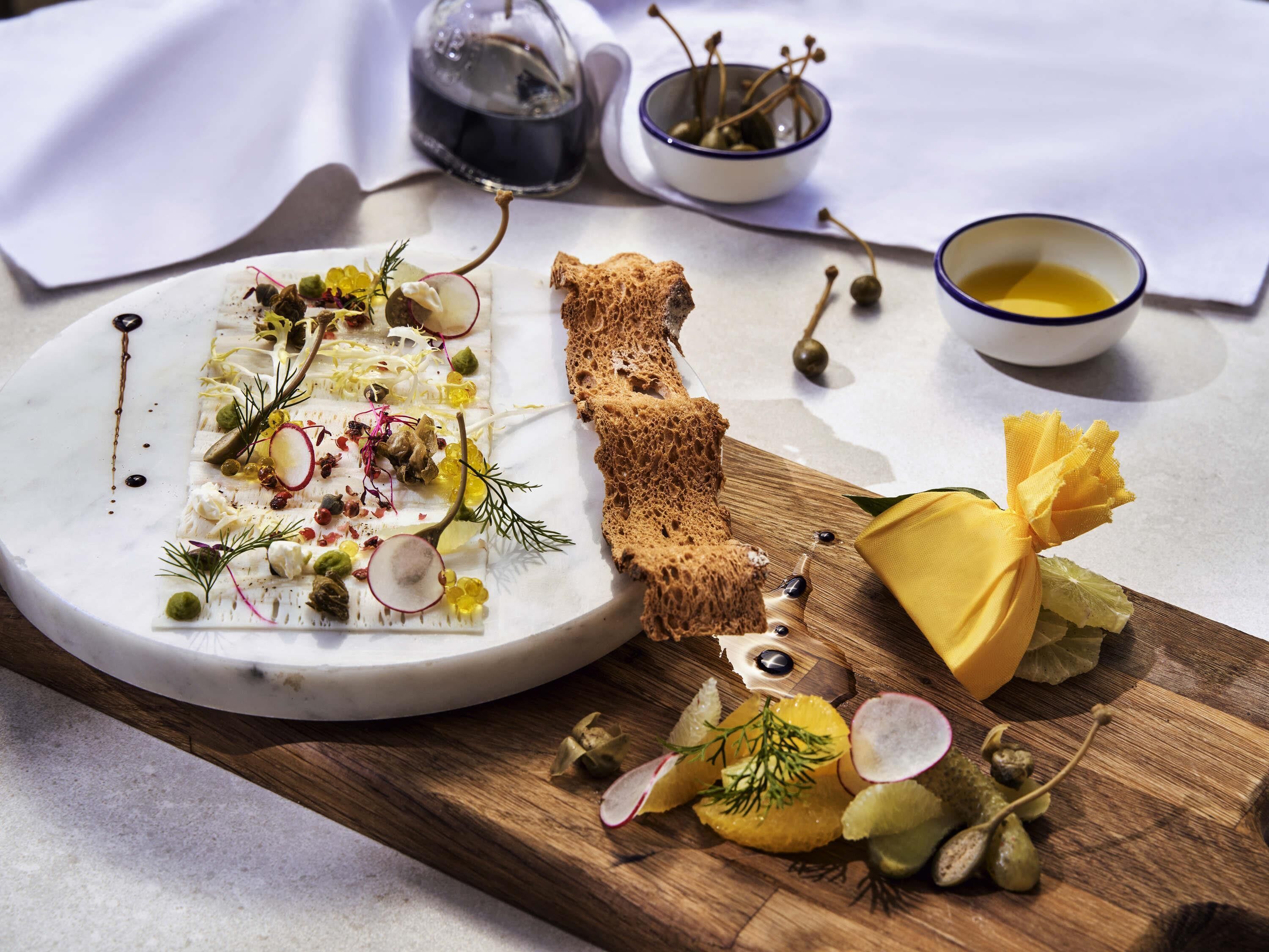 A white plate with a variety of food items, a wooden board with additional food, and two small bowls with liquid.
