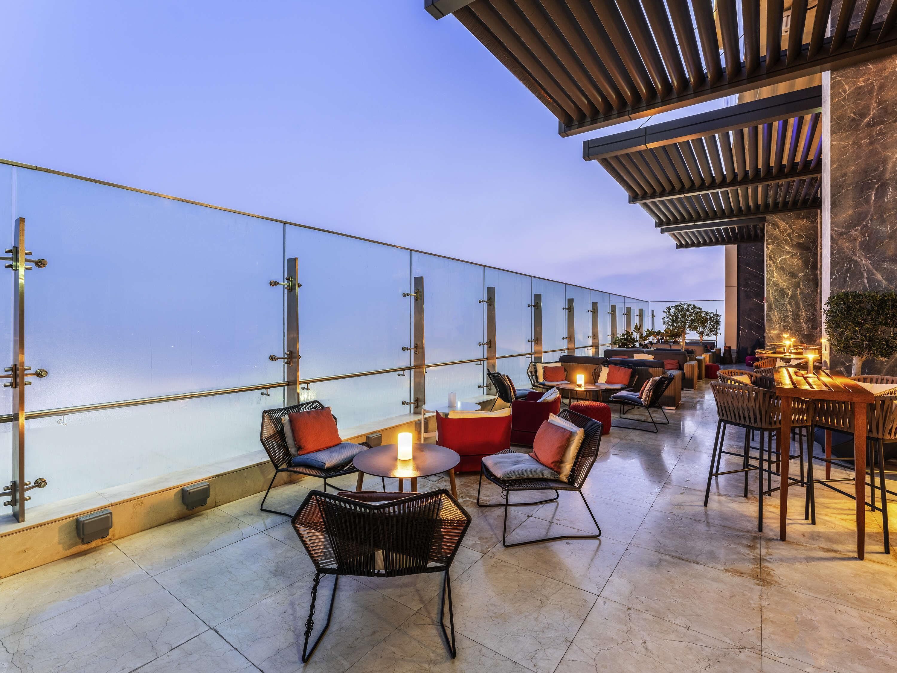 An outdoor seating area with tables and chairs, a glass railing, and a view of the ocean.