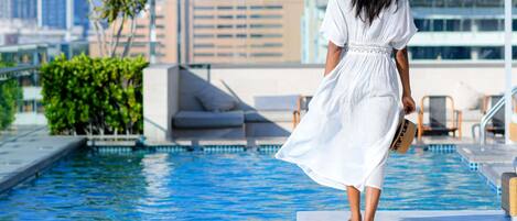 A woman in a white dress walking by a pool with a cityscape in the background.