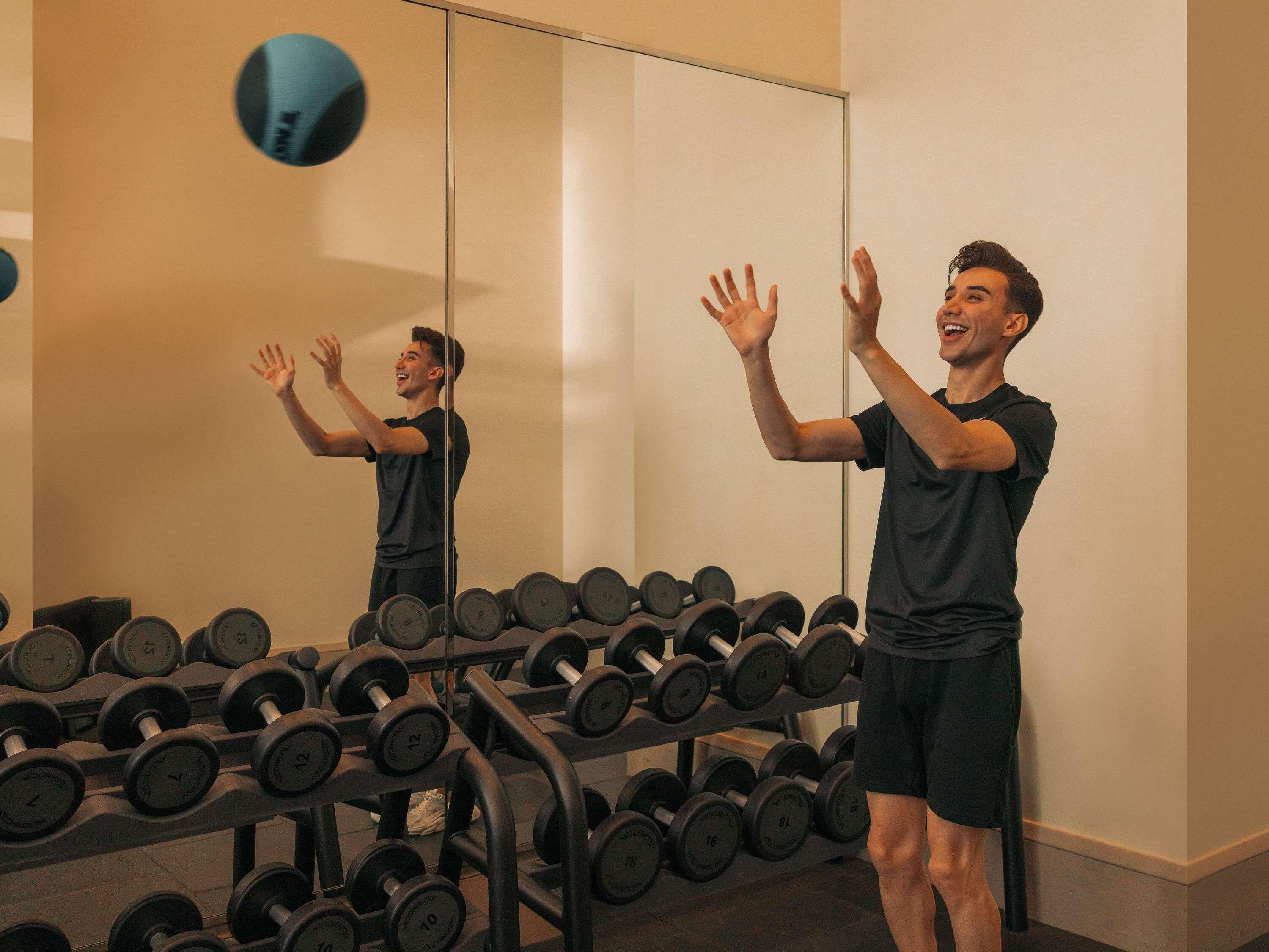 Une salle de sport avec un miroir, un porte-haltères et une personne qui s’entraîne.