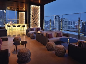 Un salon moderne avec vue sur la ville, comprenant un bar, des canapés et des tables rondes.