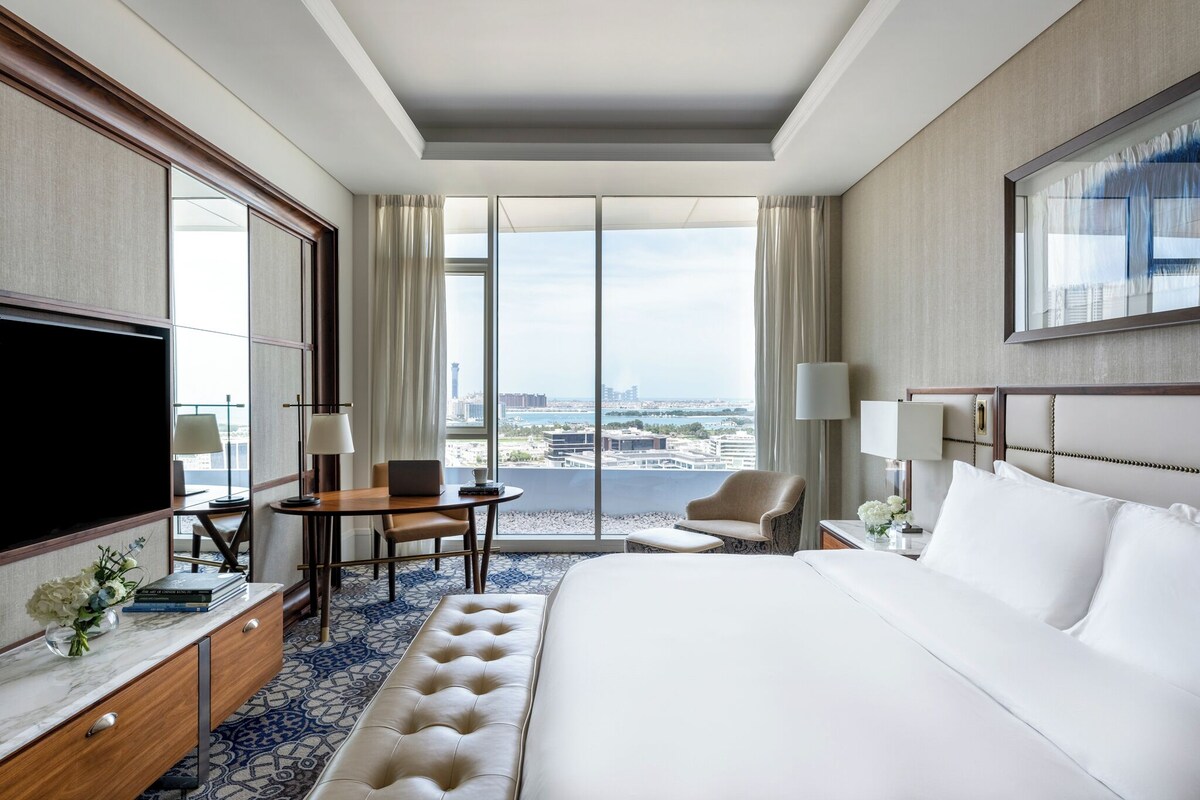 A hotel room with a large bed, a desk with a laptop, a chair, and a TV.