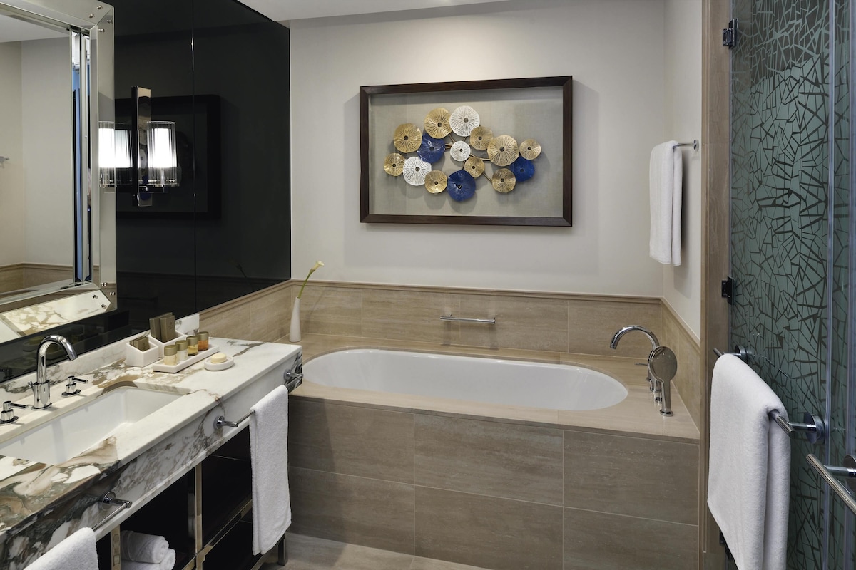 Un baño moderno con tocador de mármol, bañera independiente y un adorno mural.