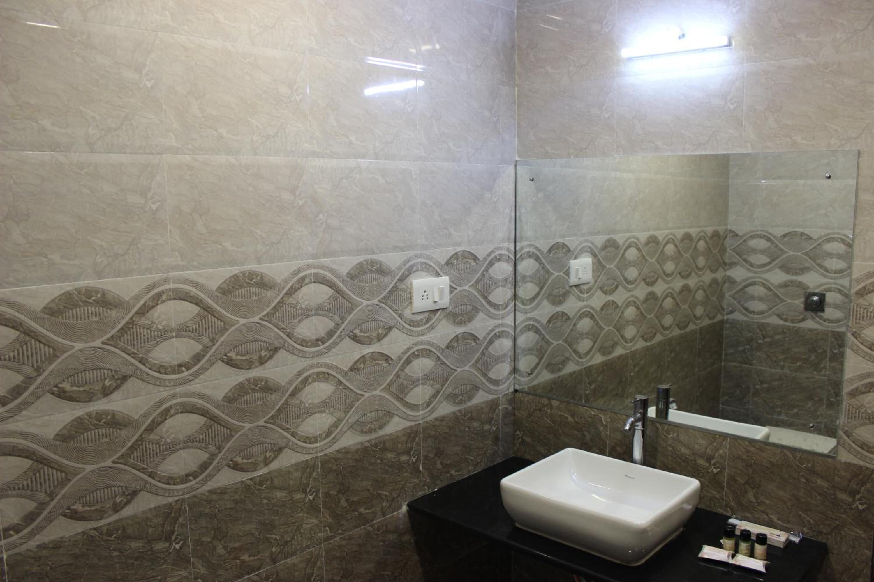 A bathroom with a rectangular sink, a mirror, and patterned tiles on the walls.