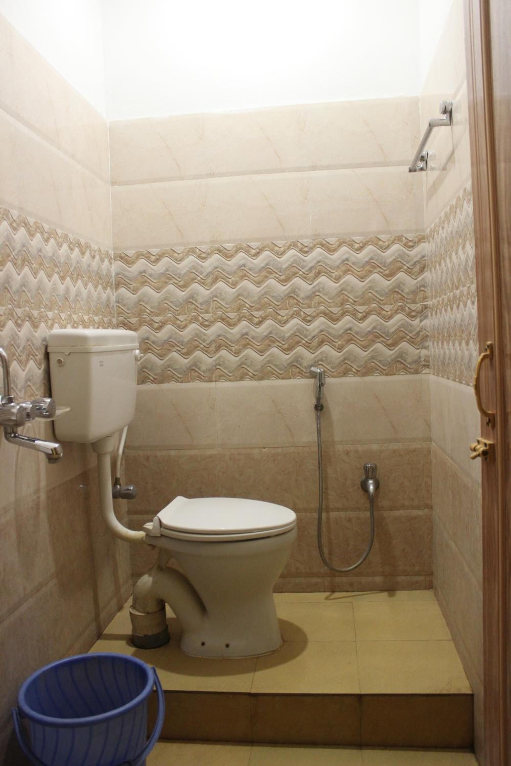 Een kleine betegelde badkamer met toilet, douche en een blauwe emmer.