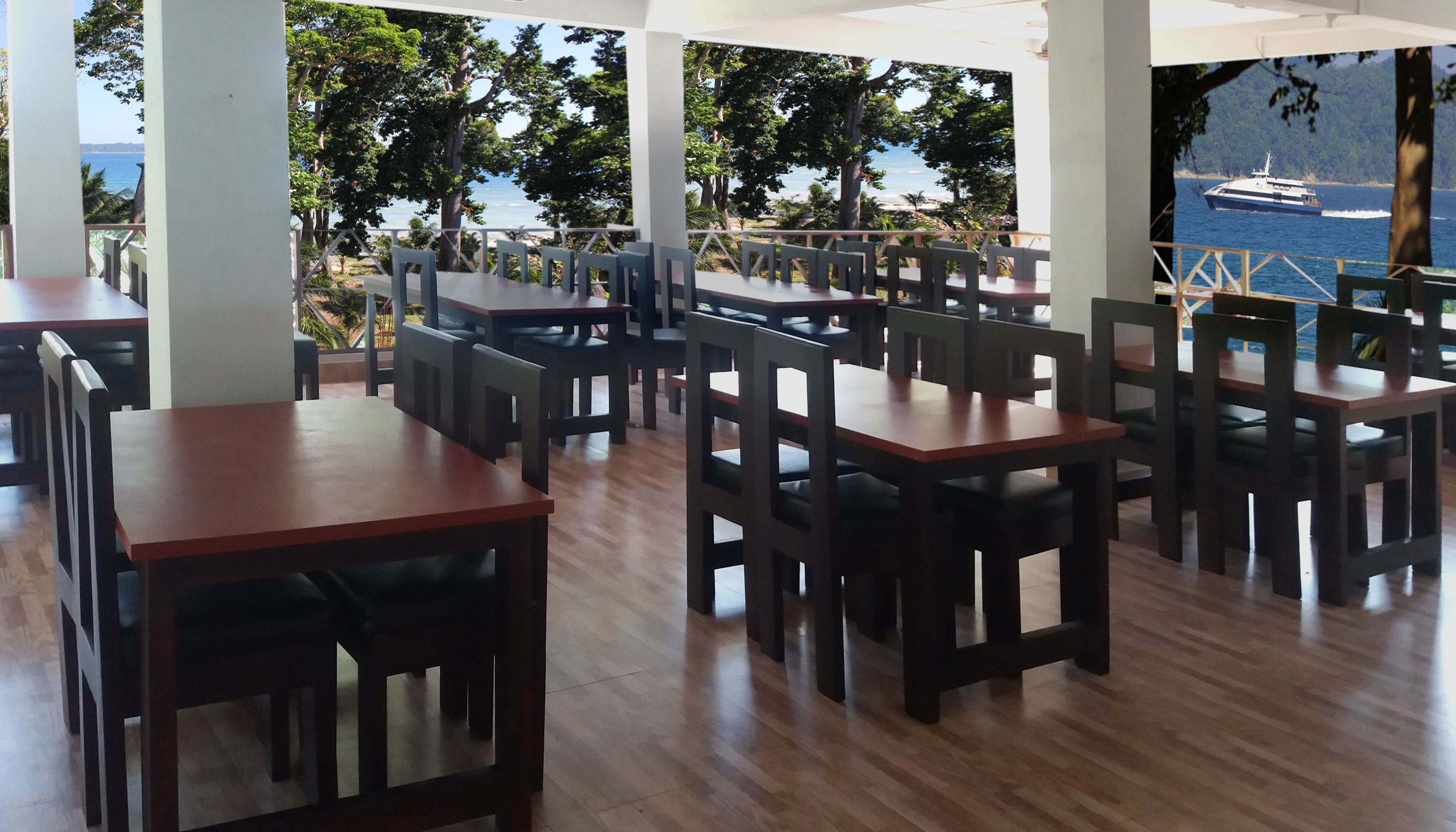 A restaurant with wooden tables and chairs, large windows offering a view of the sea and boats.