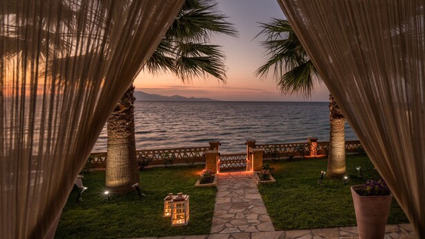 A sunset view through a curtain, a stone pathway, palm trees, and a fence leading to the sea. - Playa Del Zante (Zakynthos)