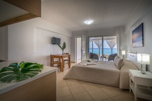 A hotel room with a bed, a desk, a chair, a TV, and a view of the sea. - Playa Del Zante (Zakynthos)
