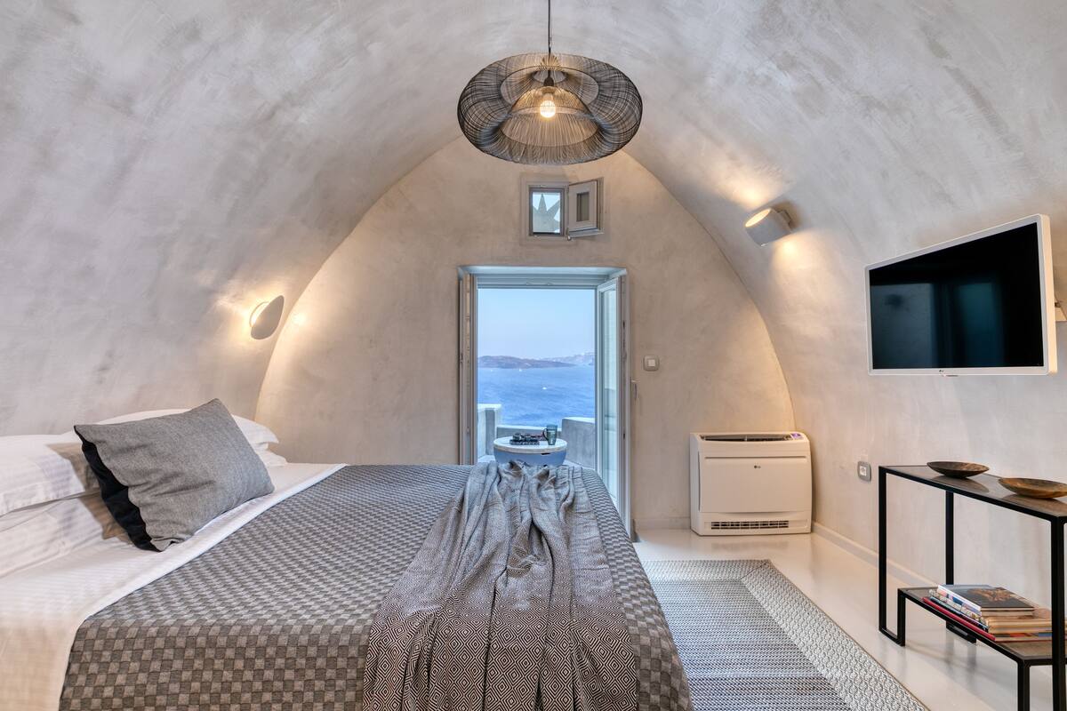 A bedroom with a bed, a TV, a small table, and a view of the sea.