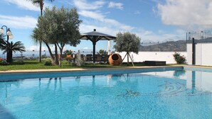 A swimming pool with clear blue water, surrounded by greenery and a white wall.
