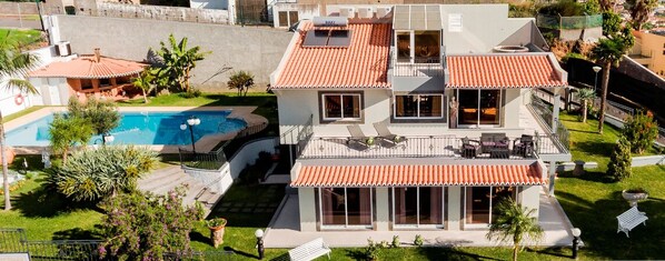Una casa a due piani con piscina, patio coperto e giardino curato.