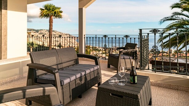 A balcony with wicker furniture, a glass table, and a view of the sea.