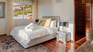 A neatly arranged bedroom with a bed, bedside table, and a view of the outside.
