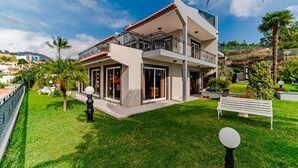 A modern two-story house with a balcony, surrounded by well-maintained grass and palm trees.