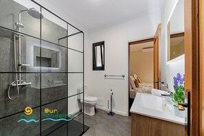 A modern bathroom with a glass shower enclosure, a toilet, and a sink area with a mirror and decorative plants.
