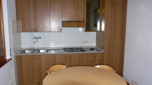 A kitchen with wooden cabinets, a sink, a stove, and a round table with chairs.