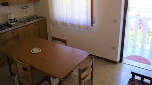 A compact kitchen with a dining area, a window with curtains, and a door leading to an outdoor area.