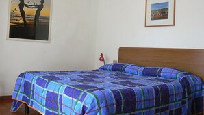 A bedroom with a bed, a painting of a couple on a beach, and a framed picture on the wall.