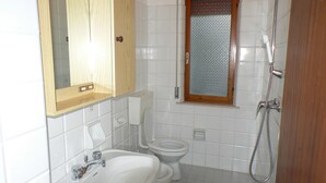 A bathroom with a wooden cabinet, a window with a metal screen, a toilet, a sink, and a shower.