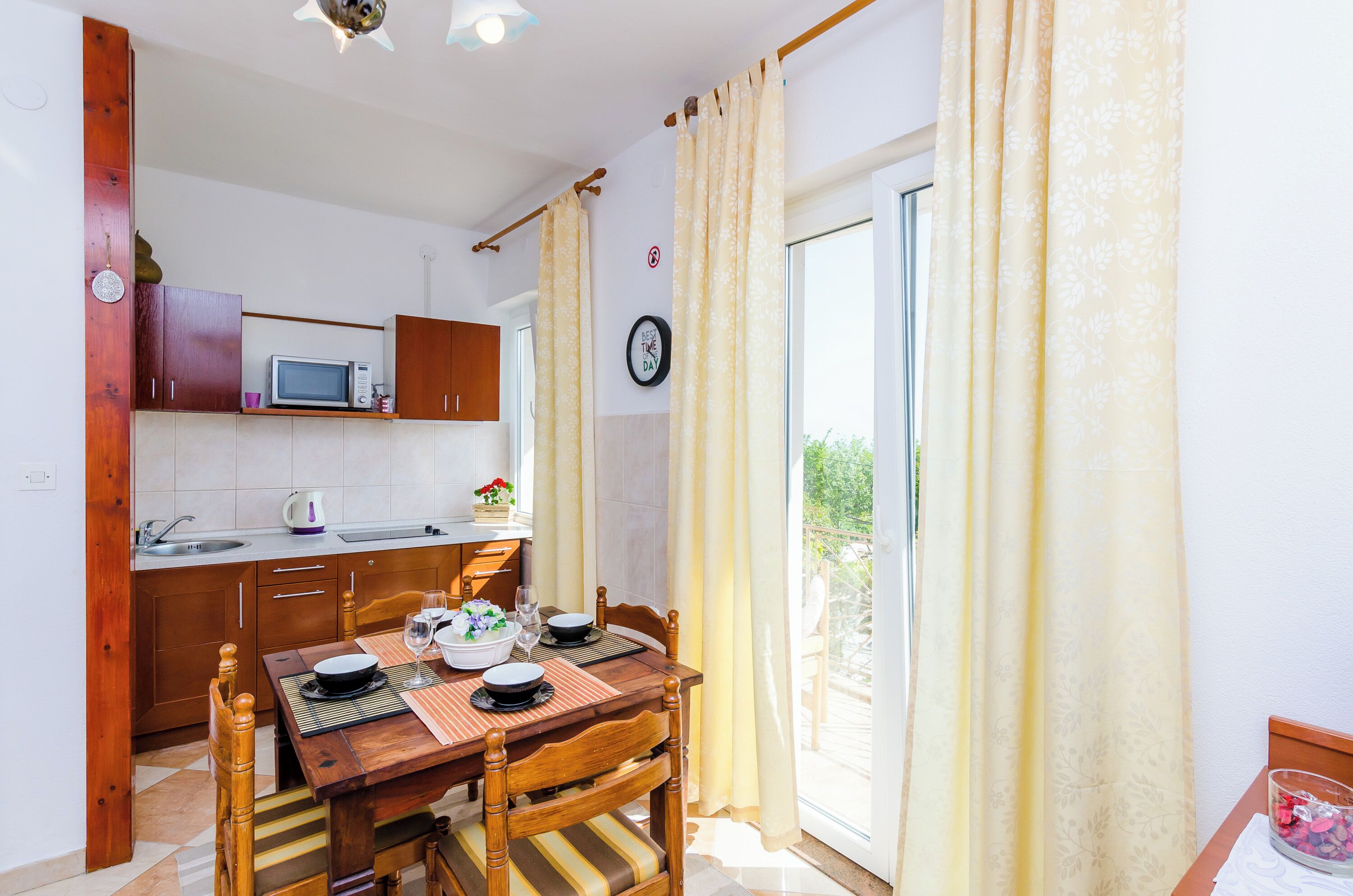 A compact kitchen with wooden cabinets, a microwave, and a dining area with a table set for two.