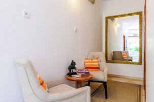 Um quarto com duas poltronas, uma mesinha com livros e uma estátua, e um espelho grande na parede.