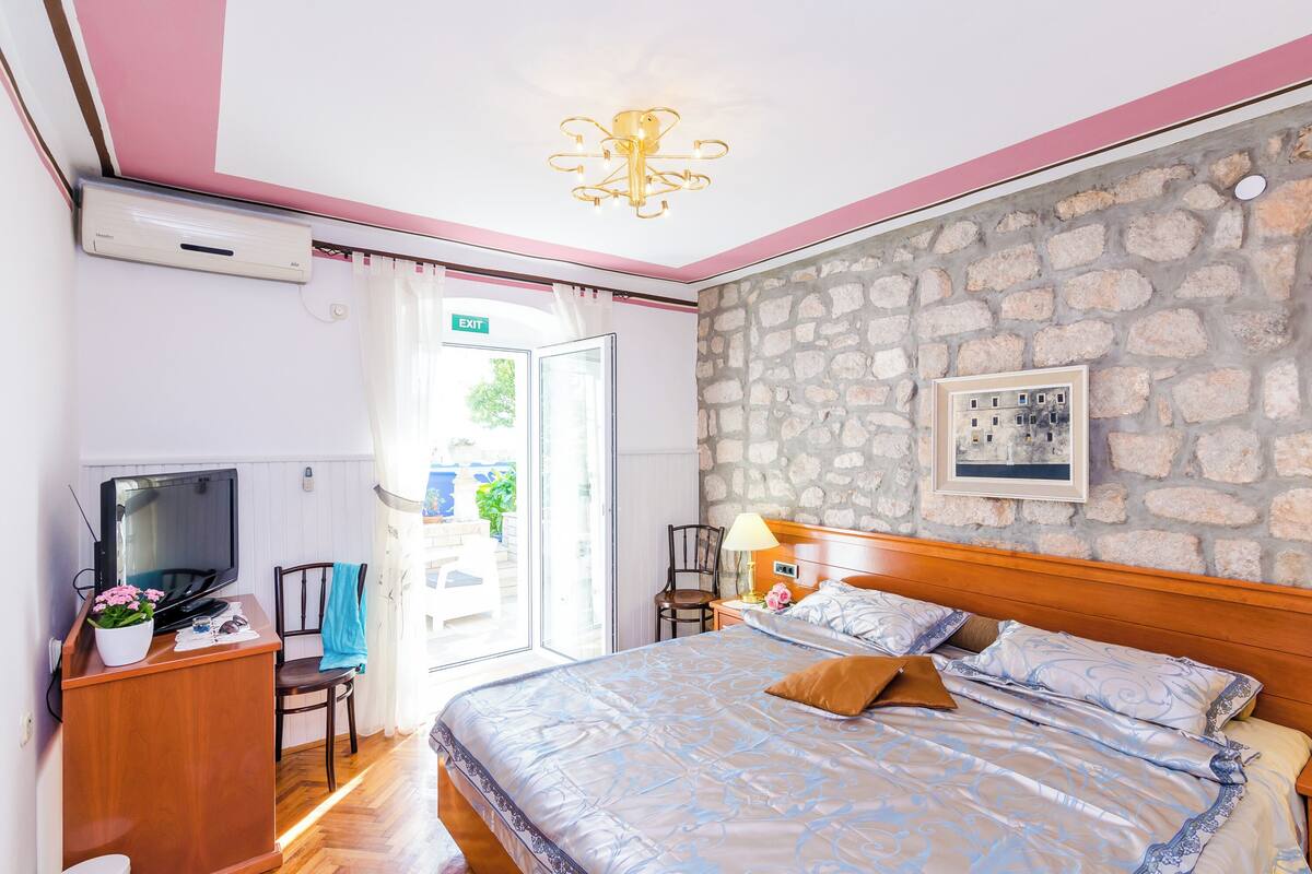 A bedroom with a bed, a TV, a desk, and a stone wall.