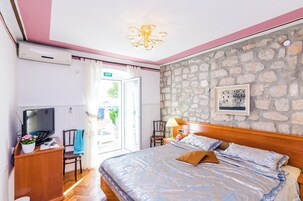 A bedroom with a bed, a TV, a desk with a computer, a chair, and a stone wall.