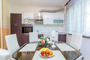 A modern kitchen with white cabinets, a built-in oven, and a dining area with a glass table and white chairs.