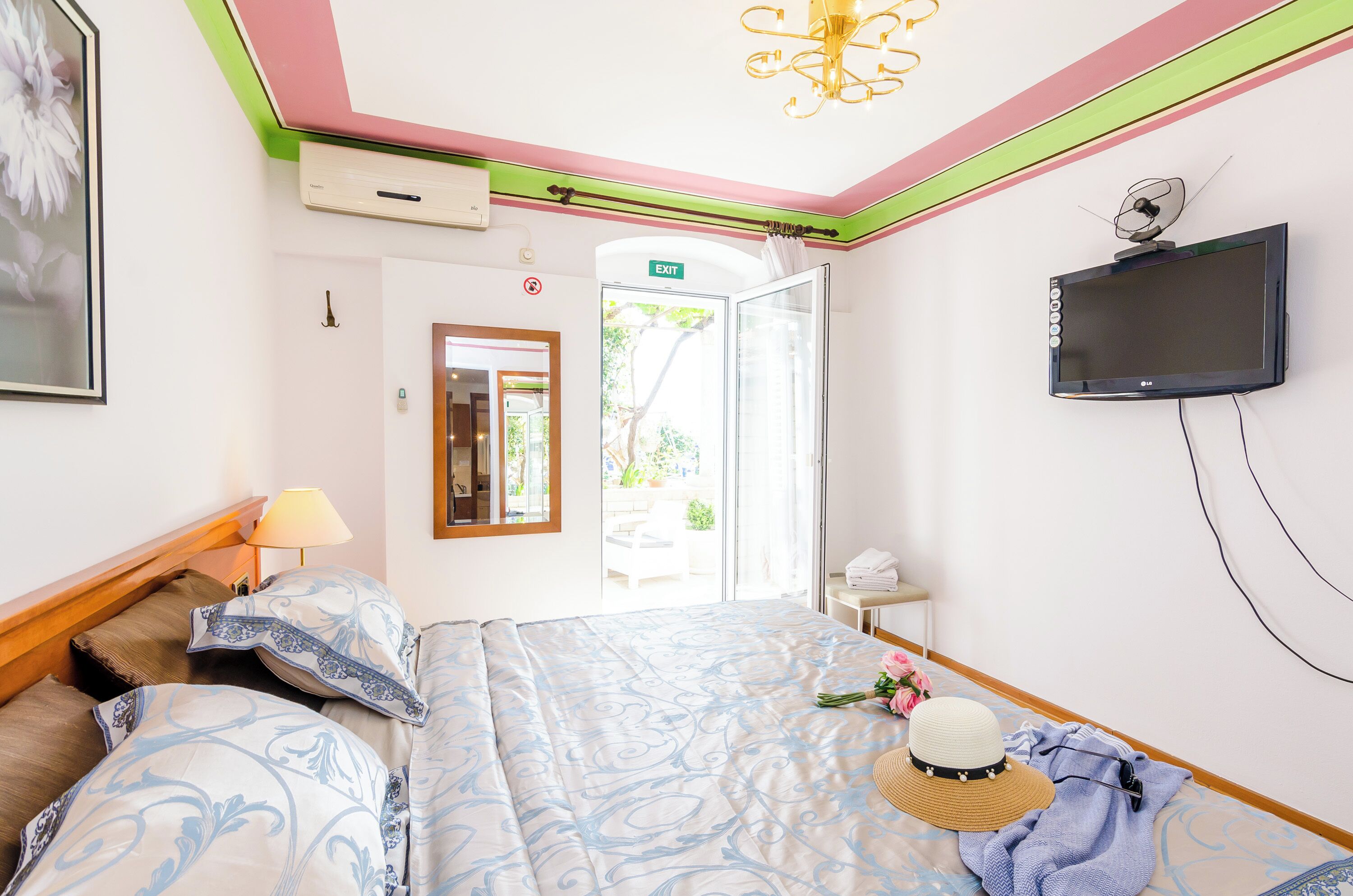 Une chambre d’hôtel avec un lit, un téléviseur fixé au mur, une fenêtre avec un panneau indiquant la sortie et une porte donnant sur l’extérieur.