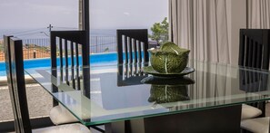 A glass-top dining table with a decorative ceramic centerpiece, black chairs, and a view of a swimming pool and buildings in the background.