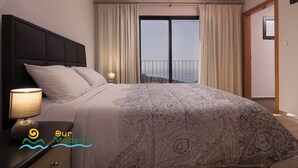 A bedroom with a large bed, a nightstand with a lamp, and a view of the sea through a balcony. - Casa da Rosalina (Calheta)