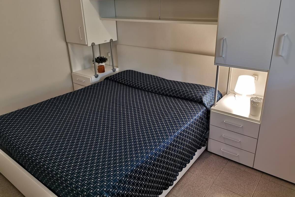 A bedroom with a bed, a nightstand, a lamp, and a wardrobe.