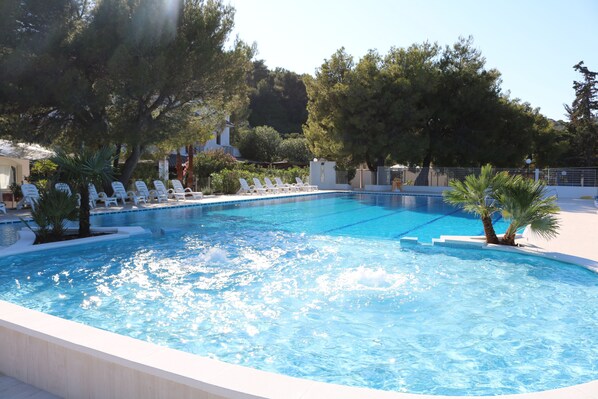 A swimming pool with clear blue water, surrounded by white lounge chairs and palm trees.
