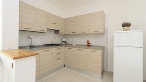 A modern kitchen with light wood cabinets, a stainless steel sink, a built-in stove, and a white refrigerator. - Residence Rubin (Lignano Sabbiadoro)