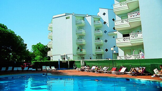 A swimming pool with lounge chairs and a multi-story building with balconies. - Residence Rubin (Lignano Sabbiadoro)