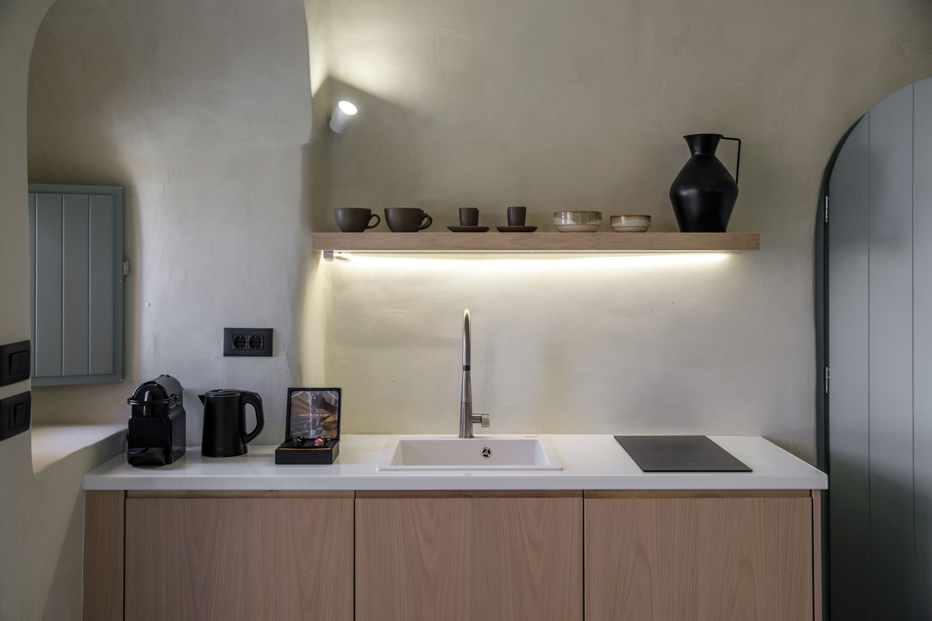 A modern kitchen with a white countertop, a built-in sink, and a shelf above it holding various kitchenware.