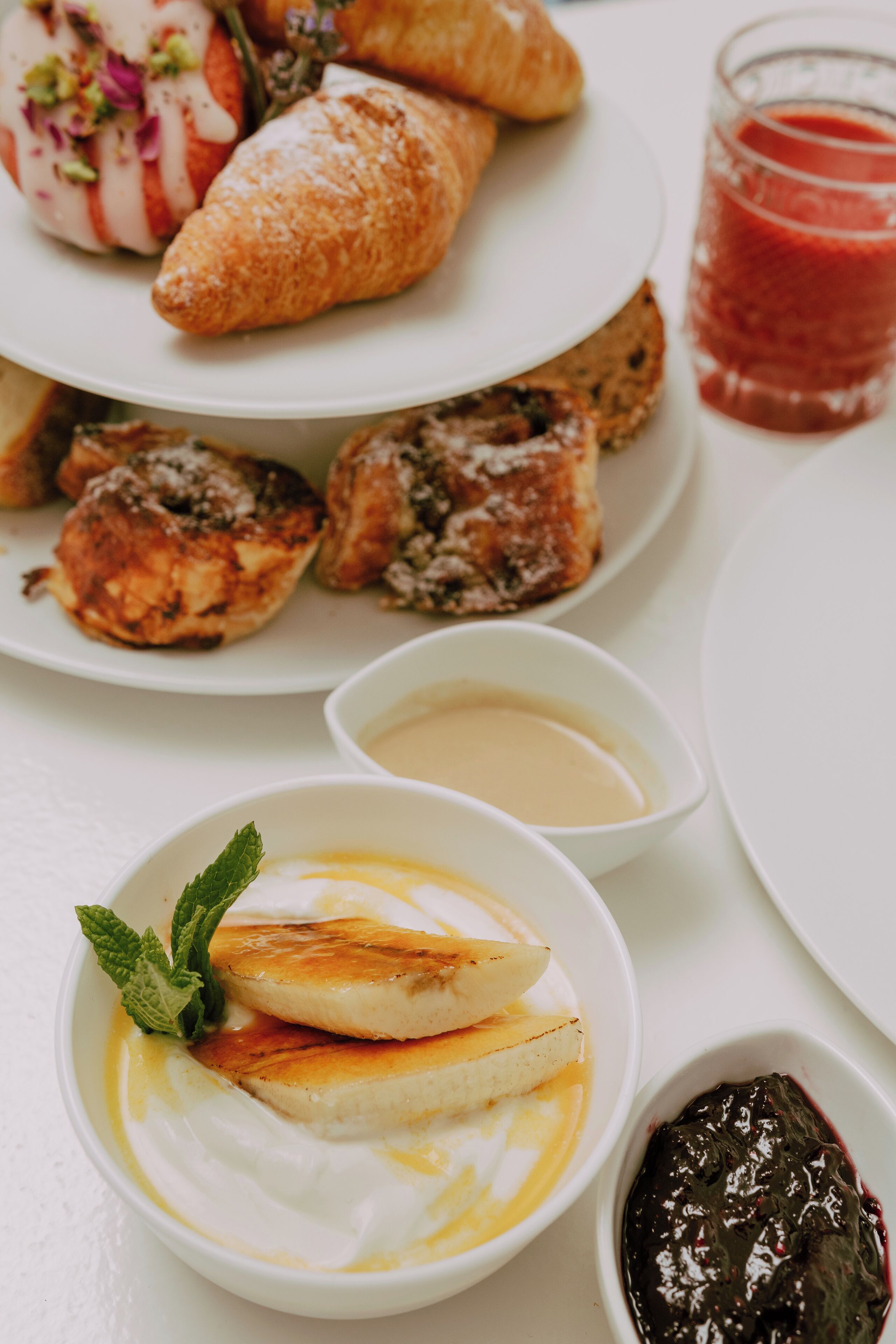 Variedad de pasteles y postres sobre una mesa blanca, incluyendo croissants, un postre con fruta y un tazón de yogur con rodajas de fruta.