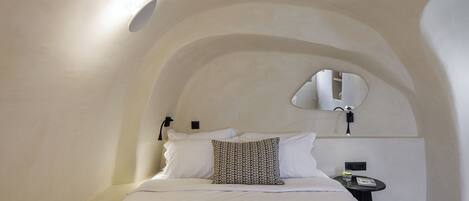 A bedroom with a bed, a bedside table, a mirror, and a wall-mounted light fixture.
