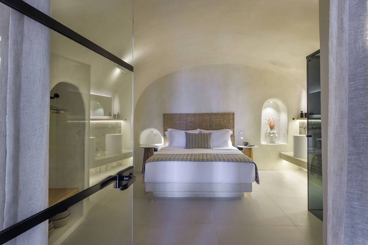 A modern hotel room with a large bed, a glass partition, and a minimalist design.