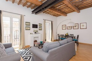 Una sala de estar con sofá, mesa de comedor, sillas, chimenea y balcón con baranda de metal.